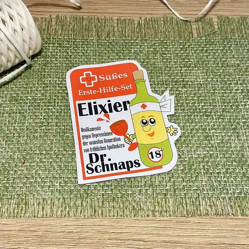 Aufkleber "Elixier Dr. Schnaps" auf einer Flasche Alkohol als Geschenk – Süßes-Erste-Hilfe-Set